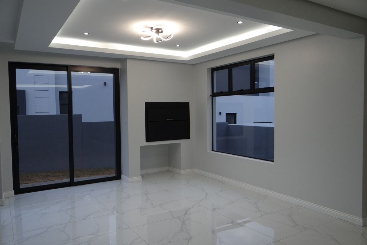 Modern living area featuring polished marble-look floor tiles, recessed tray ceiling with integrated LED lighting, and large black-framed sliding glass doors.