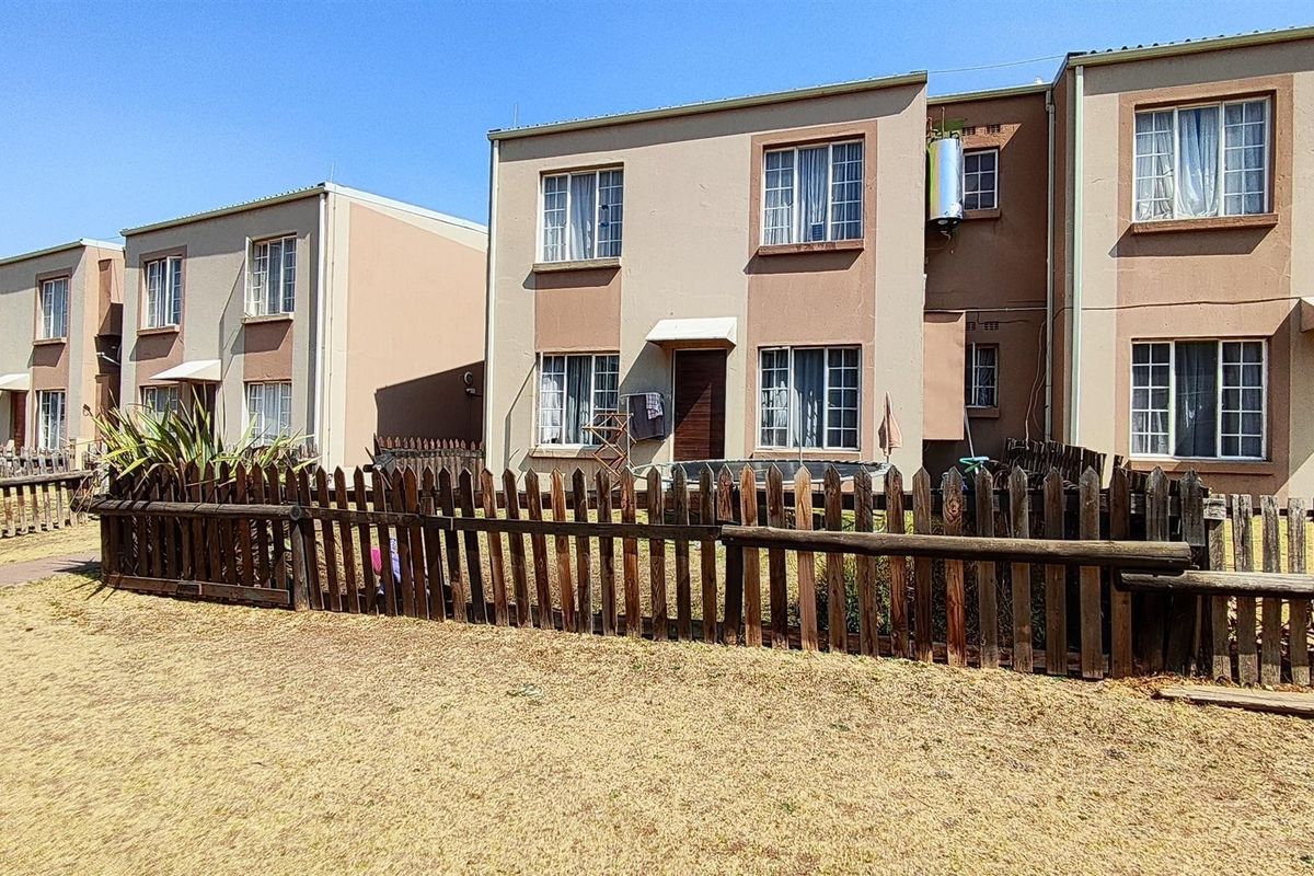 Rear view of a multi-story apartment complex featuring private garden spaces enclosed by wooden picket fencing and standard window configurations.