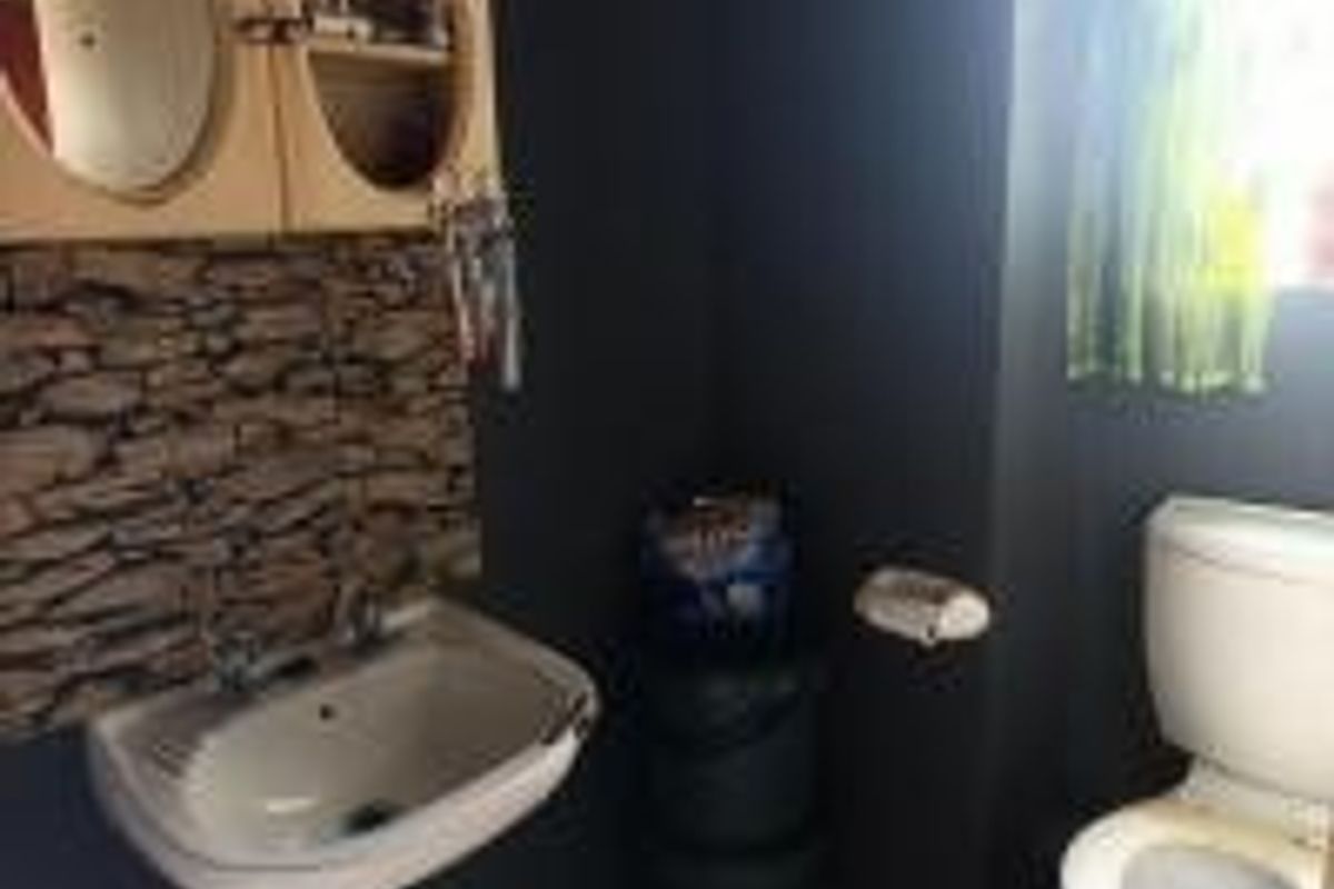 A compact bathroom featuring a wall-mounted basin with stone-effect splashback tiling and a standard toilet.