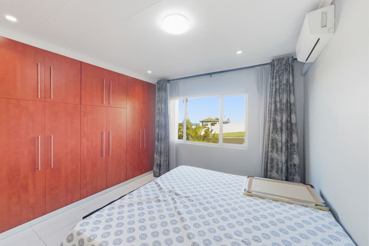 A bright bedroom featuring extensive built-in wooden cabinetry, tiled flooring, and a wall-mounted air conditioning unit with a view of the outdoors.
