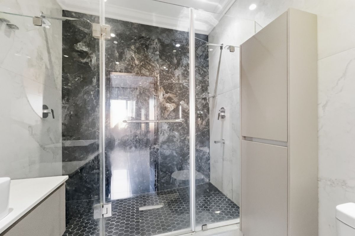 Modern bathroom featuring a walk-in glass shower enclosure with dark marble-effect wall tiles, hexagonal floor tiles, and built-in cabinetry.