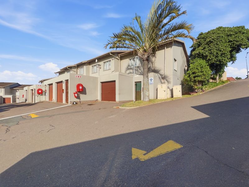 Exterior view of a townhouse complex featuring multiple garage units, paved driveway access, and established landscaping.