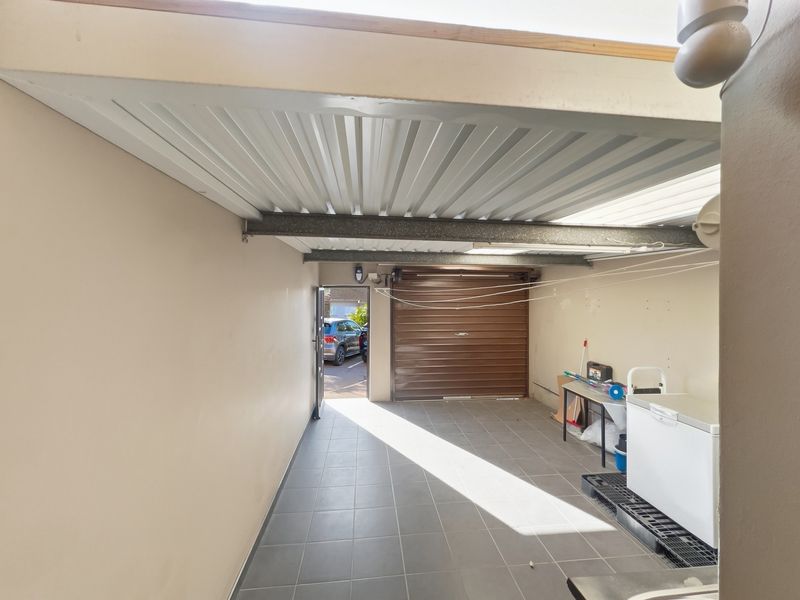 A functional garage space featuring tiled flooring, a metal roller door, and a covered patio area with direct access to the exterior.