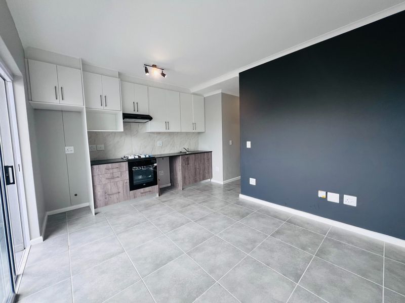 Modern open-plan kitchen and living area featuring sleek cabinetry, built-in appliances, tiled flooring, and a striking dark accent wall.