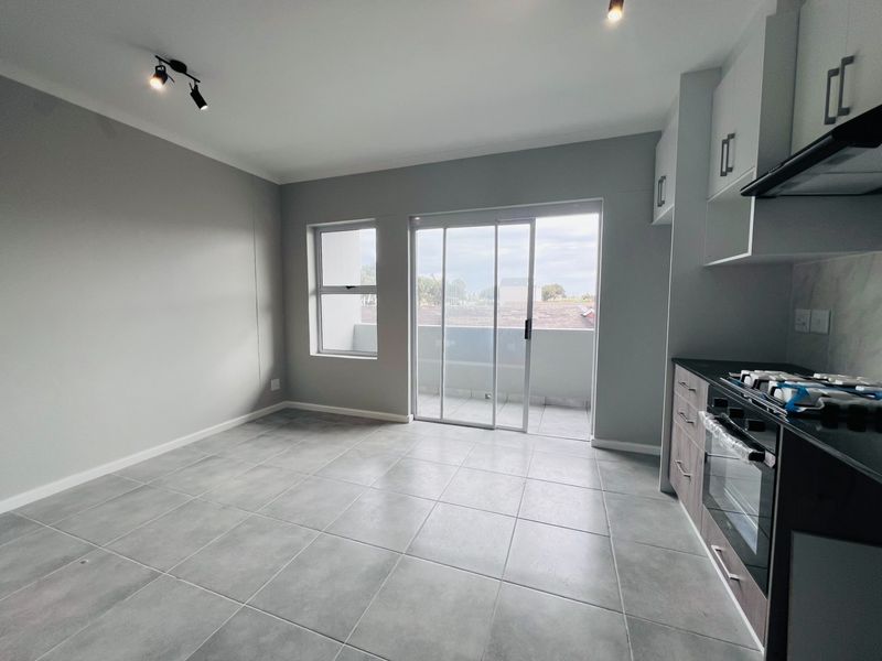 Modern open-plan living area featuring tiled floors, a sleek kitchen with built-in appliances, and sliding glass doors leading to a private balcony.