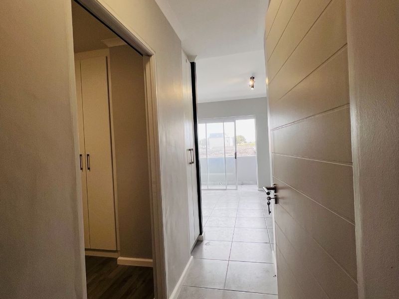 A clean, well-maintained hallway featuring neutral tiled flooring, built-in storage cupboards, and a view through to an adjacent living area with a sliding door.
