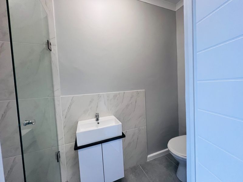Modern bathroom featuring a vessel sink with vanity cabinet, toilet, and a glass-enclosed shower with marble-look wall tiling.