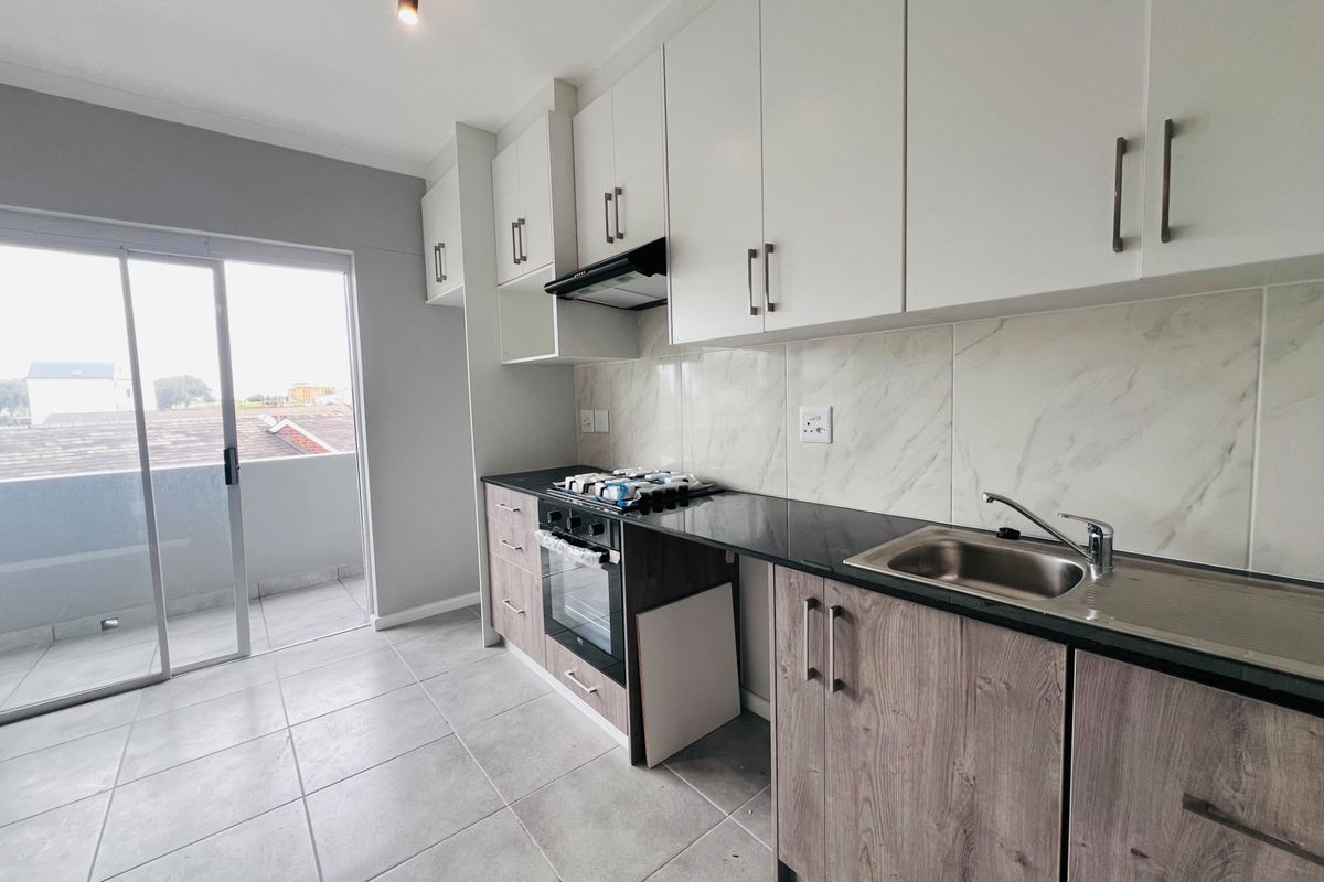 Modern kitchen featuring white upper cabinets, wood-grain lower cabinetry, black granite countertops, built-in oven, gas hob, and direct access to a balcony.