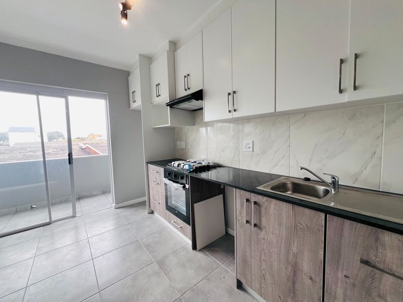 Modern kitchen featuring white upper cabinets, wood-grain lower cabinetry, black granite countertops, built-in oven, gas hob, and direct access to a balcony.