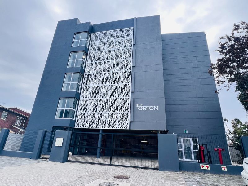 Modern apartment building facade featuring a decorative metal screen, secure gated entrance, and paved driveway access.