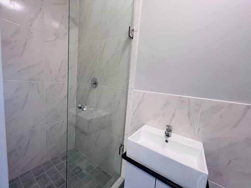 Modern bathroom featuring a glass-enclosed shower with marble-look wall tiles and a contemporary wall-mounted basin with chrome fixtures.