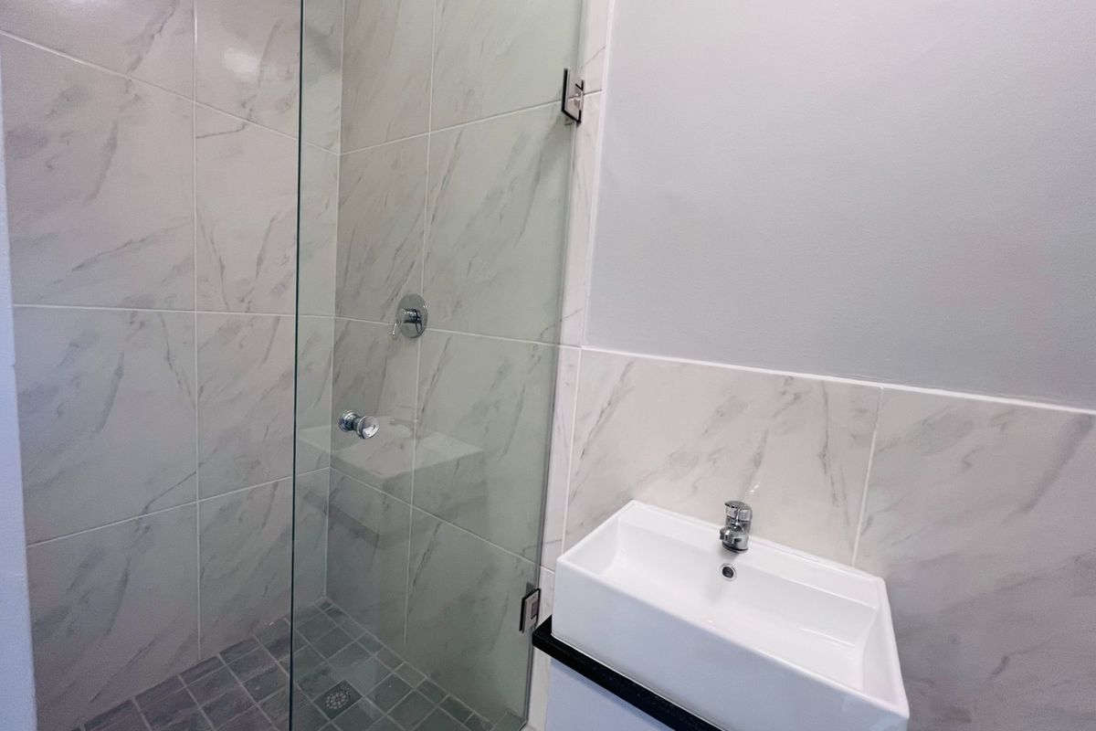 Modern bathroom featuring a glass-enclosed shower with marble-look wall tiles and a contemporary wall-mounted basin with chrome fixtures.