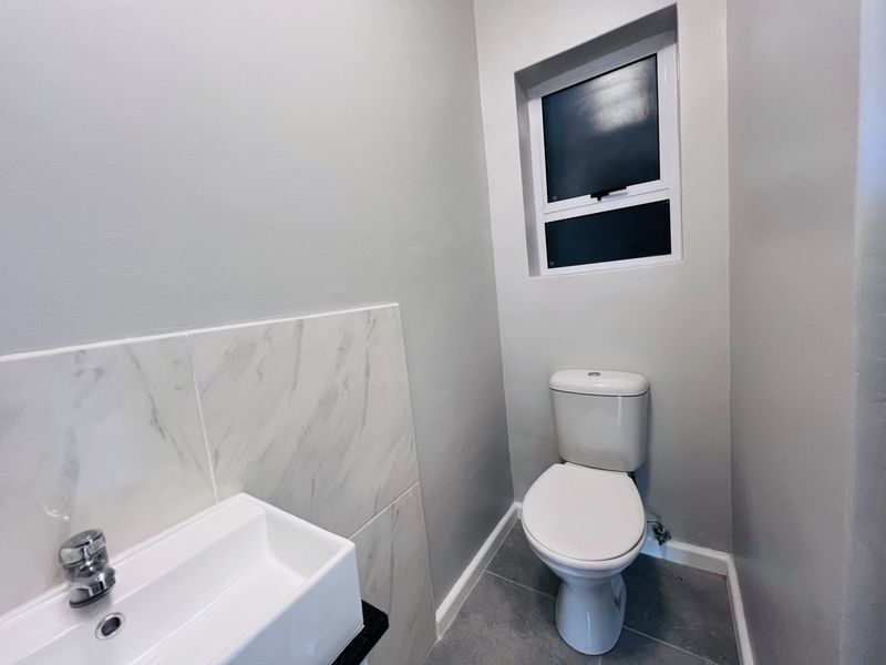 A clean, modern guest bathroom featuring a white toilet, a contemporary basin with chrome faucet, and marble-look wall tiling.