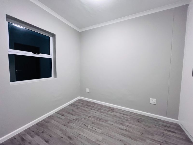 A clean, empty bedroom featuring neutral grey walls, modern laminate wood-look flooring, and a single window, providing a versatile blank canvas for any interior style.