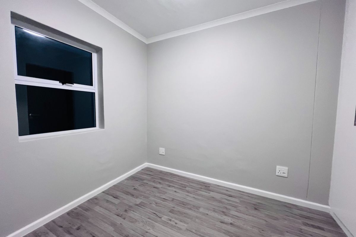 A clean, empty bedroom featuring neutral grey walls, modern laminate wood-look flooring, and a single window, providing a versatile blank canvas for any interior style.