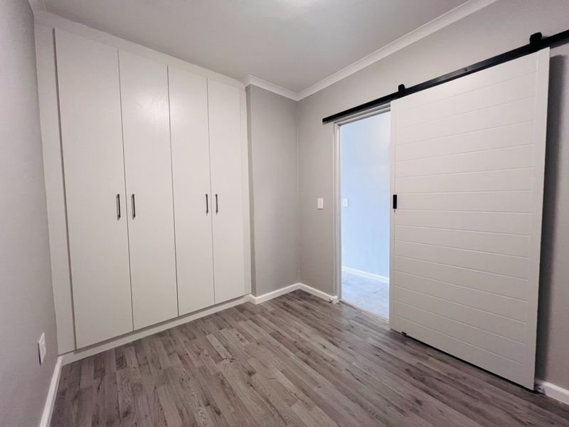 A clean, modern bedroom featuring light-toned laminate flooring, ample built-in cupboard storage, and a contemporary white sliding barn door.