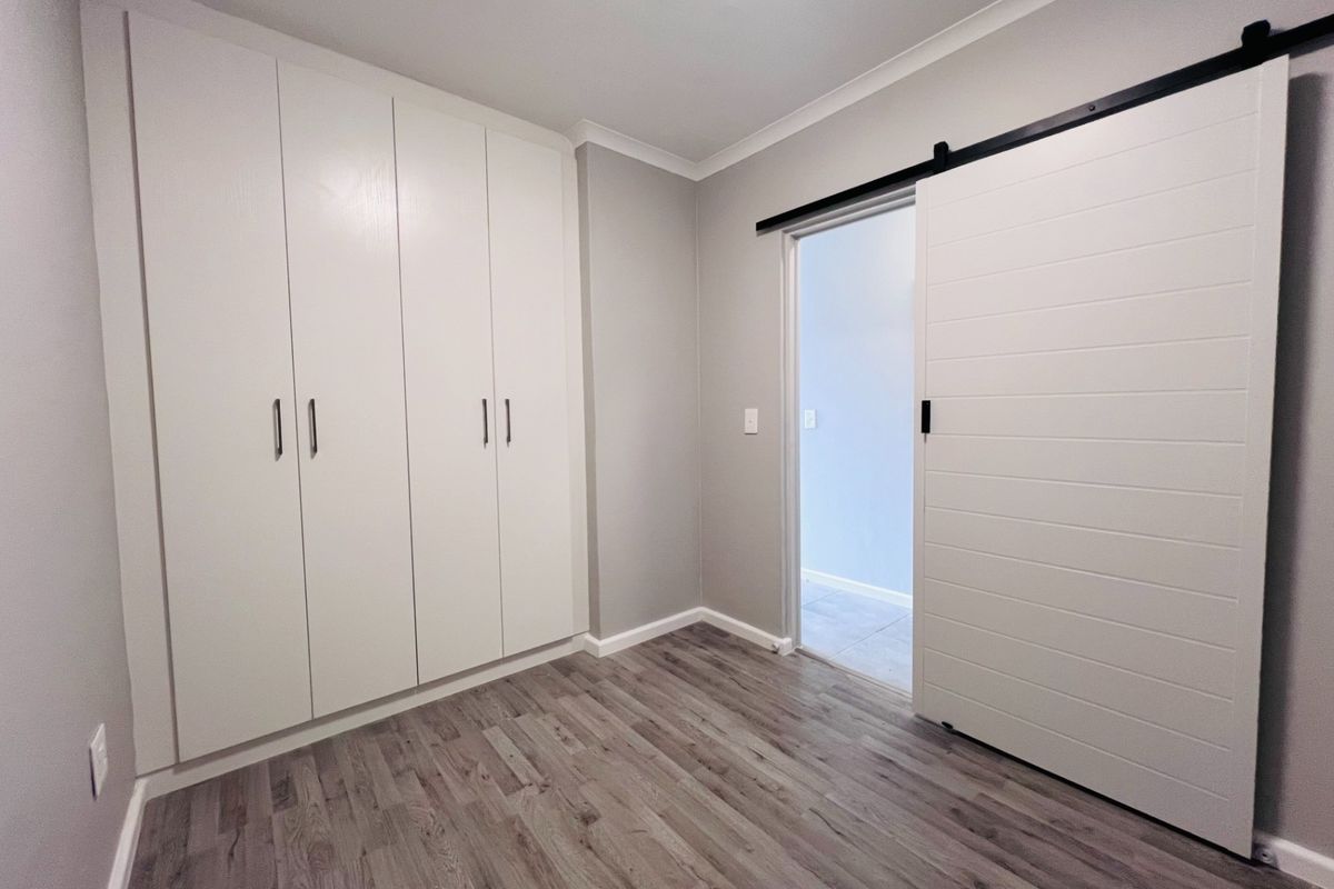 A clean, modern bedroom featuring light-toned laminate flooring, ample built-in cupboard storage, and a contemporary white sliding barn door.