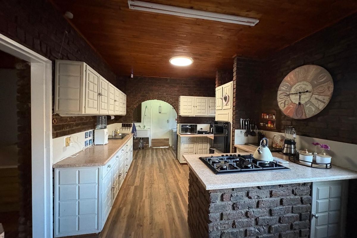 Rustic kitchen featuring exposed brick walls, timber ceiling, white cabinetry, and a central island with a built-in gas hob.