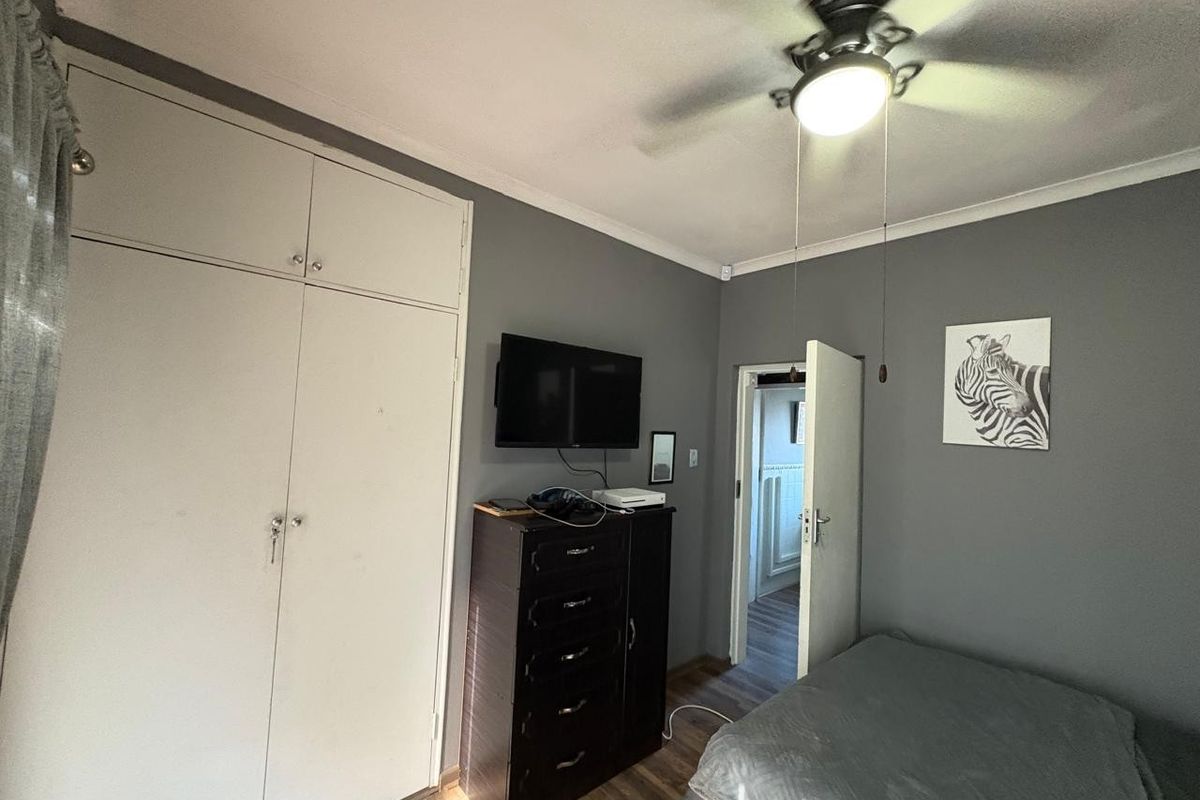 A bedroom featuring built-in cupboards, a ceiling fan with integrated lighting, and laminate flooring.