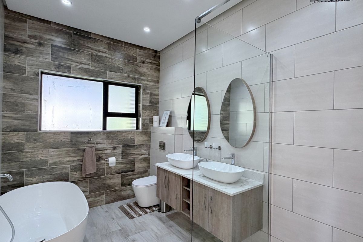 Modern bathroom featuring a freestanding bathtub, double vanity with vessel sinks, glass-enclosed shower, and contemporary wood-look tile finishes.
