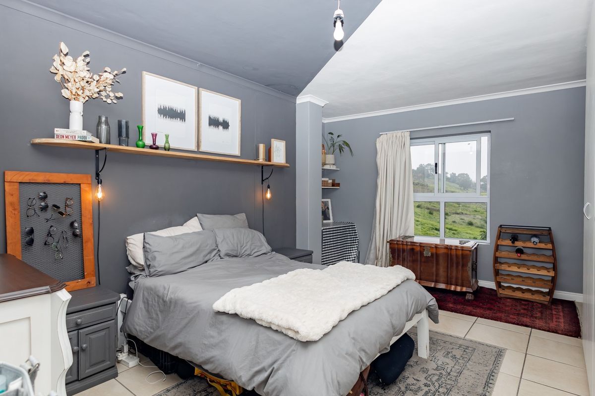 A well-maintained bedroom featuring neutral grey walls, tiled flooring, built-in cupboards, and a large window offering scenic views of the surrounding landscape.