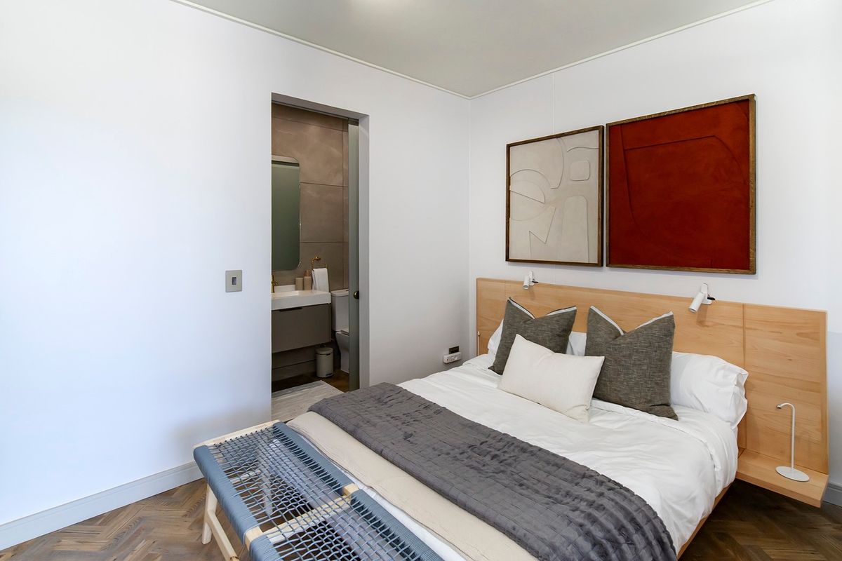 Modern bedroom featuring elegant herringbone timber flooring, a custom built-in headboard with integrated lighting, and direct access to a private en-suite bathroom.