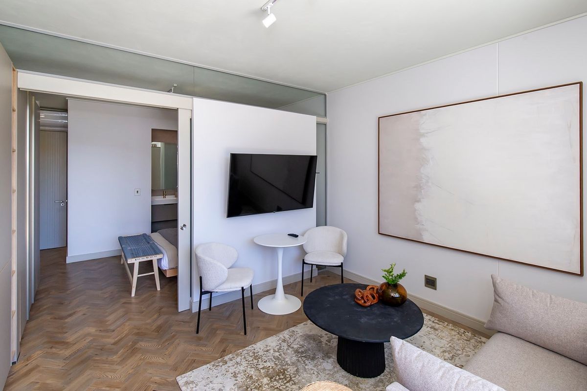 A modern living room featuring elegant herringbone timber flooring, a sliding door leading to the bedroom, and clean, minimalist wall finishes.