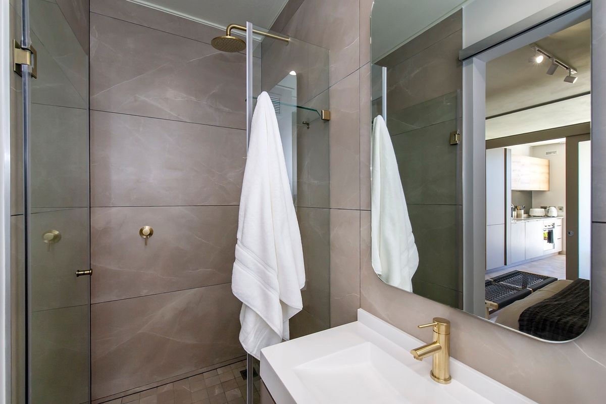 Modern bathroom featuring large format wall tiles, a walk-in shower with a rain shower head, and elegant brass fixtures.