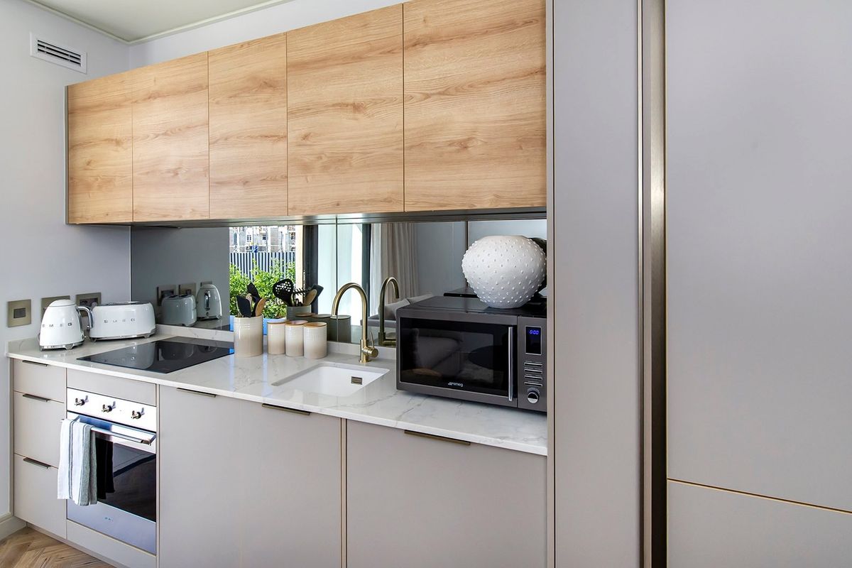 Modern kitchen featuring light wood-grain upper cabinetry, sleek grey lower cabinets, stone countertops, mirrored splashback, and high-end integrated appliances.