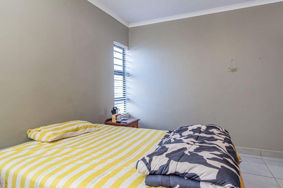 A functional bedroom featuring neutral wall tones, tiled flooring, and a window fitted with horizontal blinds.