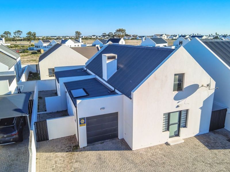 Aerial view of a modern residential property featuring a pitched roof, integrated garage, paved driveway, and surrounding estate homes.