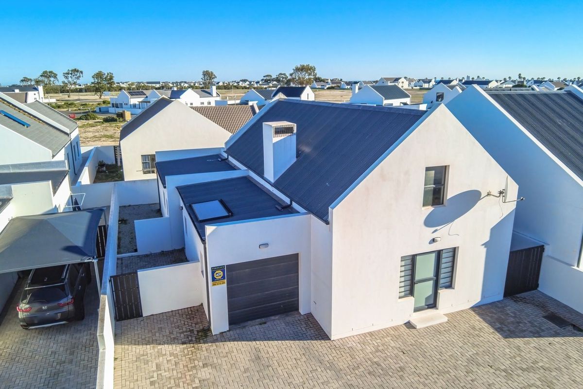 Aerial view of a modern residential property featuring a pitched roof, integrated garage, paved driveway, and surrounding estate homes.
