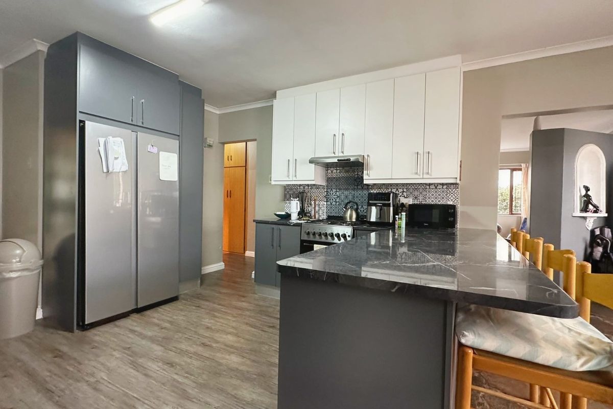 Modern kitchen featuring a central island with stone countertop, two-tone cabinetry, patterned tile backsplash, and integrated stainless steel appliances.