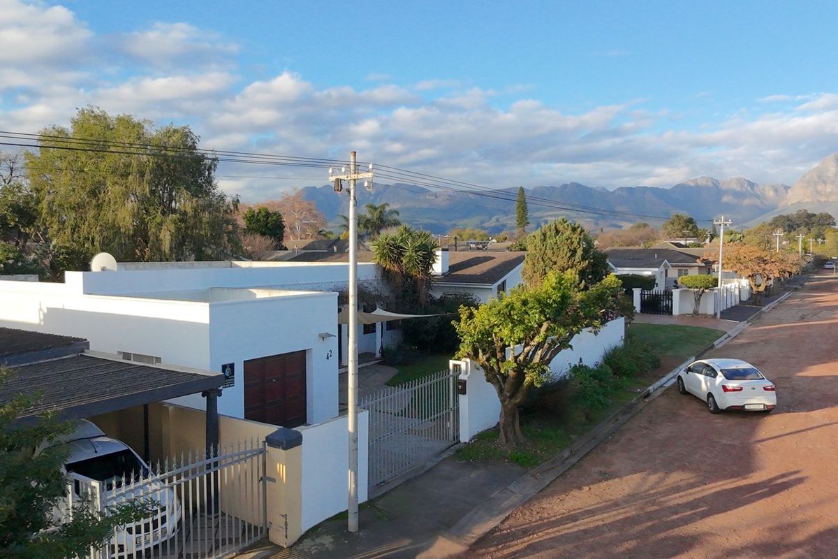 Aerial view of the property showing the front facade, driveway, perimeter wall, and surrounding neighbourhood with mountain views.