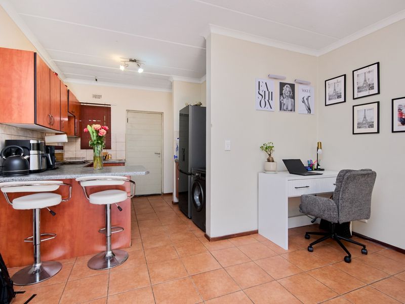 Open plan kitchen featuring wooden cabinetry, tiled flooring, and a breakfast bar, seamlessly flowing into a versatile living or workspace area.