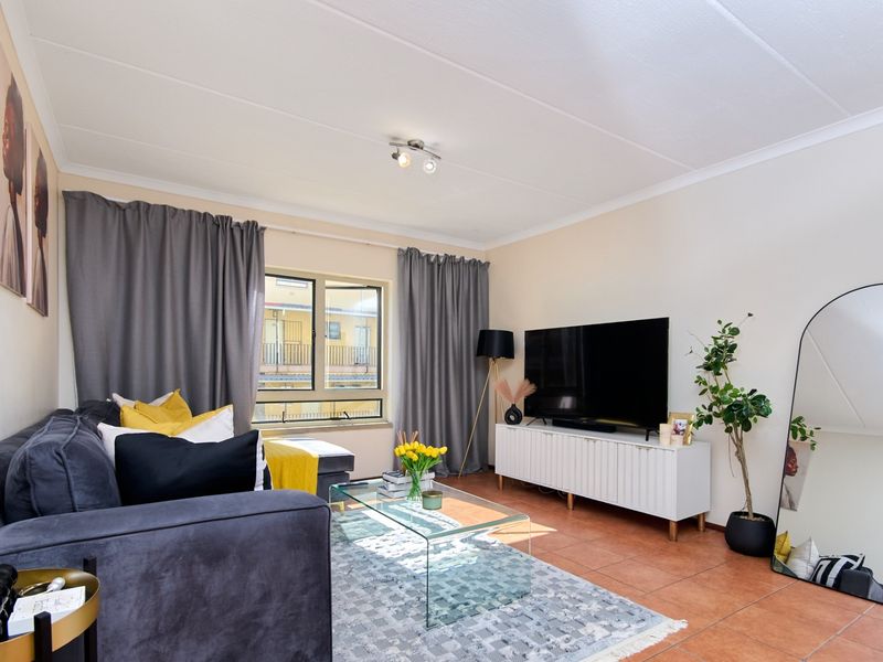 A well-lit living room featuring tiled flooring, neutral walls, and a large window with curtain treatments, providing a comfortable and functional living space.