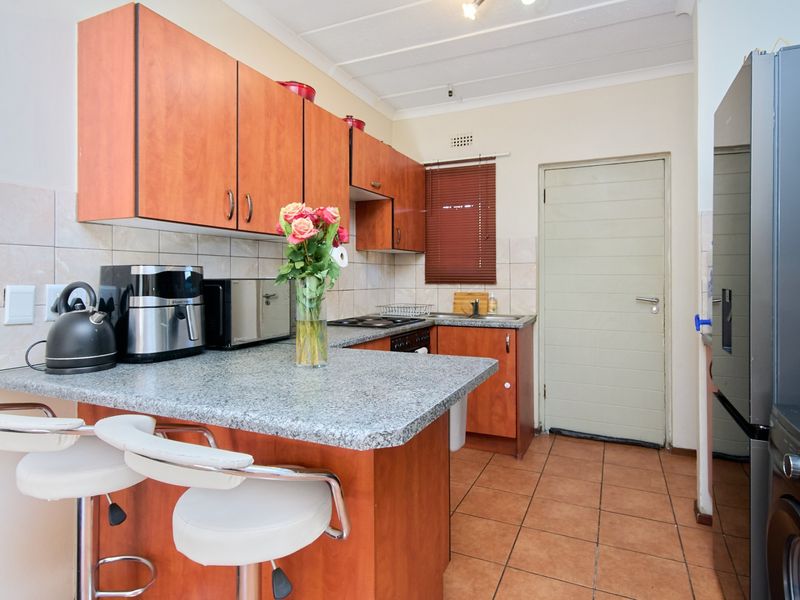 Functional kitchen featuring wood-finish cabinetry, granite-look countertops, a breakfast nook, and tiled flooring with direct access to an exterior door.