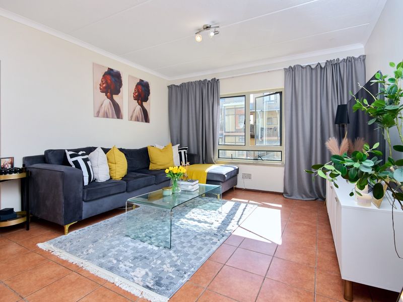A bright living room featuring terracotta floor tiles, neutral walls, and a large window with grey curtains, providing a comfortable and functional living space.