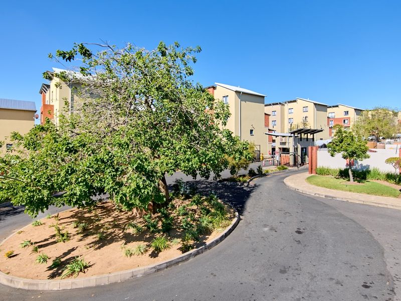 View of the apartment complex entrance, featuring a paved driveway, landscaped roundabout, and secure gated access point.