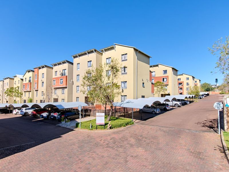 Exterior view of a multi-story apartment complex featuring paved parking areas with covered carports and landscaped grounds.