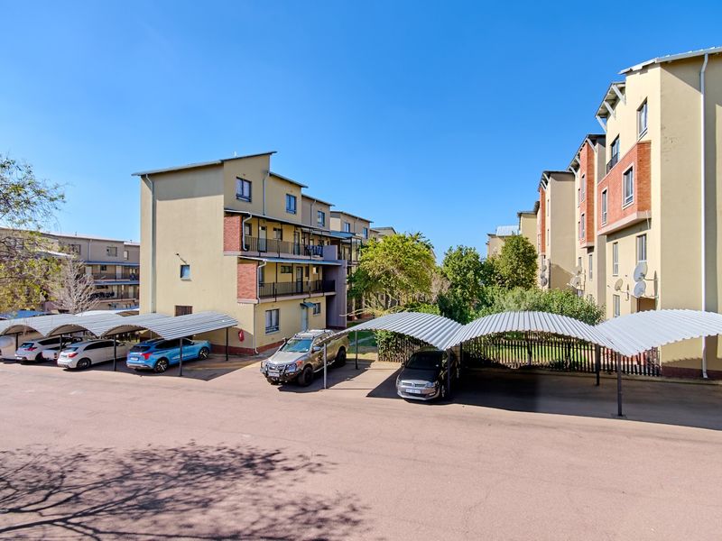 Exterior view of the apartment complex featuring paved parking areas with covered carports and multi-story residential buildings.