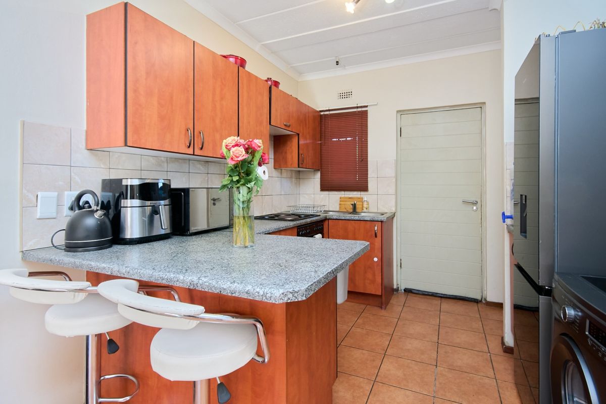 Functional kitchen featuring wood-finish cabinetry, granite-look countertops, a breakfast nook, and tiled flooring with direct access to an exterior door.