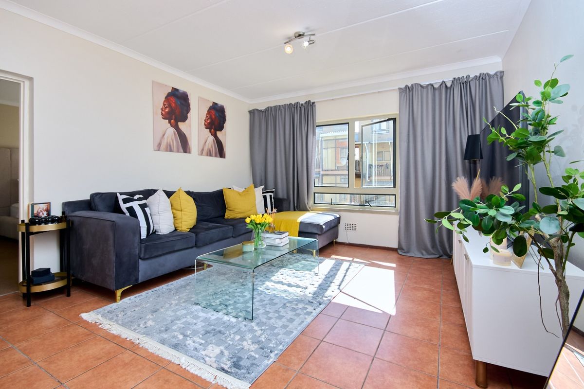 A bright living room featuring terracotta floor tiles, neutral walls, and a large window with grey curtains, providing a comfortable and functional living space.