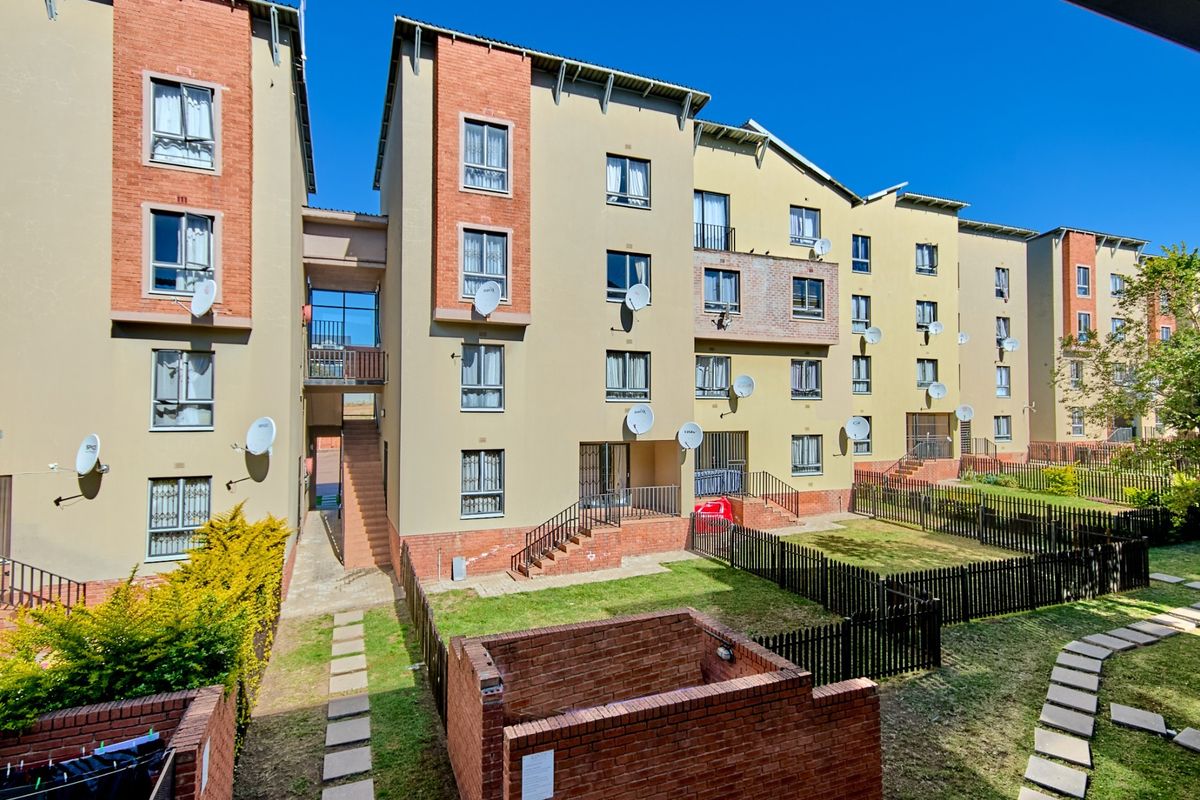 Exterior view of a multi-story apartment complex featuring brick and plaster facade, communal garden areas, and paved walkways.