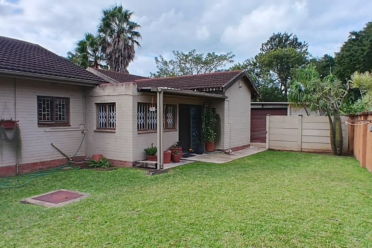 A view of the rear exterior of the house featuring a lawn, a small covered patio area, and a perimeter boundary wall.