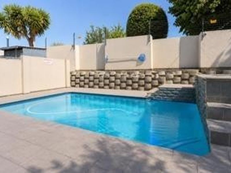 A private swimming pool area featuring paved surrounds, tiered retaining walls, and perimeter boundary fencing.
