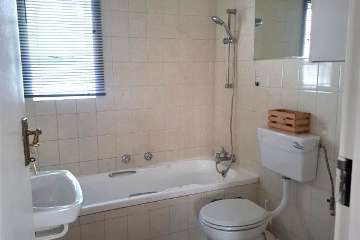 A functional bathroom featuring a bathtub with a handheld shower attachment, a wall-mounted basin, and a standard toilet with a high-level cistern.