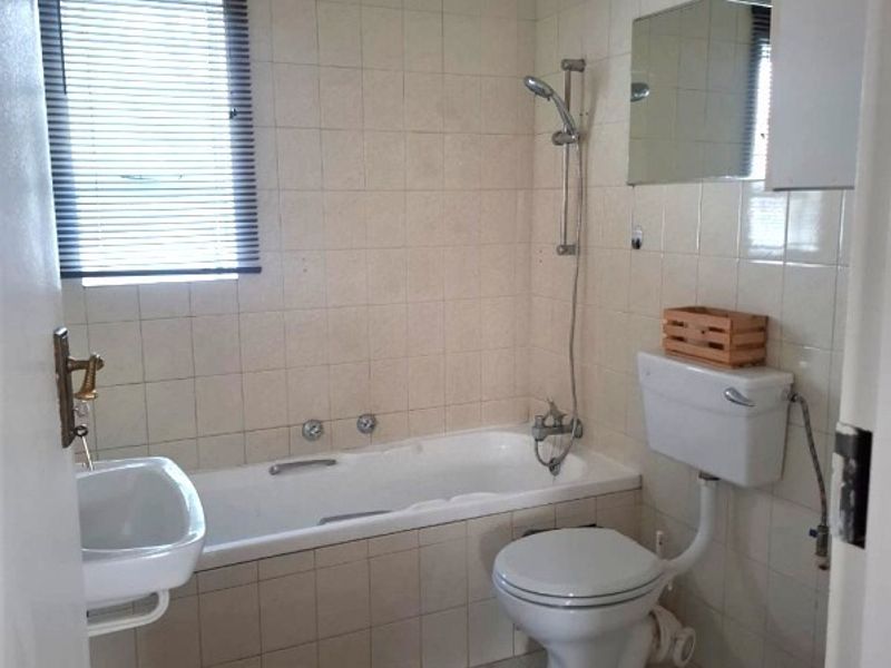 A functional bathroom featuring a bathtub with a handheld shower attachment, a wall-mounted basin, and a standard toilet with a high-level cistern.