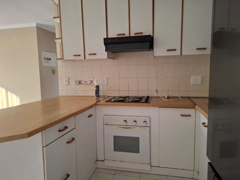 A functional kitchen featuring white cabinetry, a built-in oven, electric hob, extractor fan, and a tiled backsplash with a breakfast bar counter.