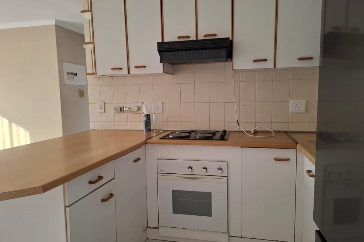 A functional kitchen featuring white cabinetry, a built-in oven, electric hob, extractor fan, and a tiled backsplash with a breakfast bar counter.
